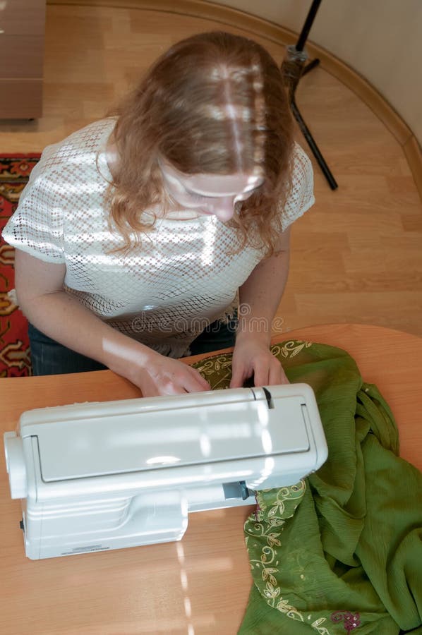 Costureira que senta-se na tabela de madeira com máquina de costura, pano e trabalho fotografia de stock Costureira que senta-se na tabela de madeira com máquina de costura, pano e trabalho fotografia de stock