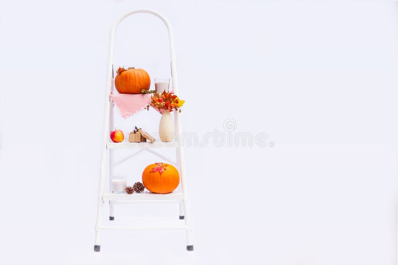 Cosy composition with natural decor of pumpkins, candles, fall leaves in vase, cones and nuts on the steps of rung ladder on white stock photo Cosy composition with natural decor of pumpkins, candles, fall leaves in vase, cones and nuts on the steps of rung ladder on white stock photo