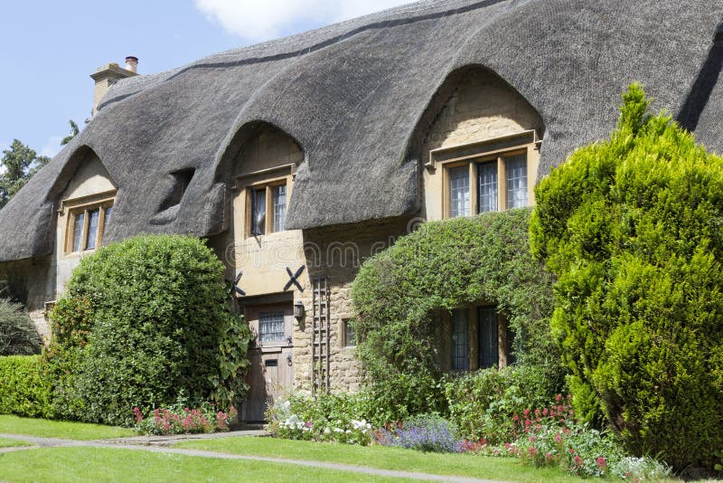 Cottage ricoperto di paglia del tetto con il giardino di fioritura in una campagna inglese fotografia stock Cottage ricoperto di paglia del tetto con il giardino di fioritura in una campagna inglese fotografia stock