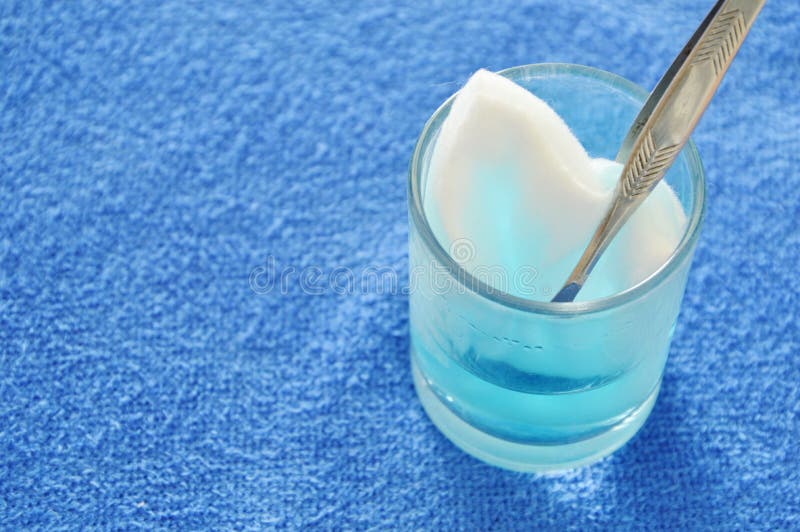 Cotton wool with tweezers picking in blue hydrogen peroxide on the glass. Cotton wool with tweezers picking in blue hydrogen peroxide on the glass