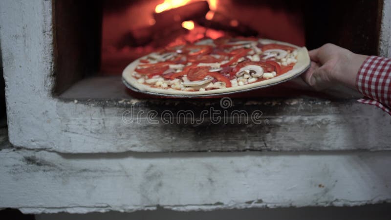 Cottura di pizza in un fuoco aperto in un forno di legna. una mano femmina mette la pizza alla mozzarella nel forno in una pentola