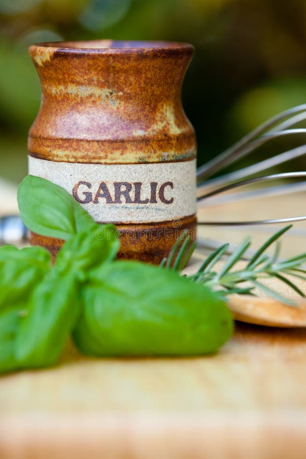 Close up of earthenware garlic pot with herbs and utensils in background. Close up of earthenware garlic pot with herbs and utensils in background