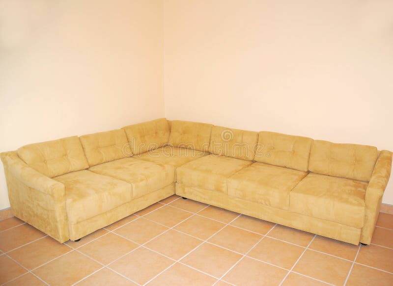 A plain beige corner sofa standing a tiled and empty room. A plain beige corner sofa standing a tiled and empty room