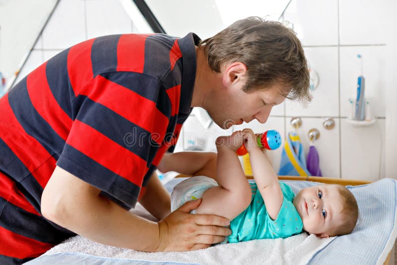 Couche-culotte changeante de père affectueux de sa fille nouveau-née de bébé image stock Couche-culotte changeante de père affectueux de sa fille nouveau-née de bébé image stock