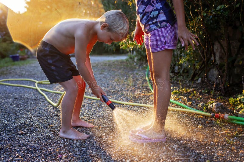 Coucher de soleil jouer avec tuyau d'eau. les frères et soeurs jouent avec l'eau au coucher du soleil image stock