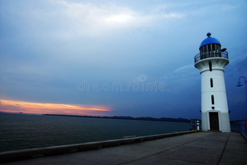 A lighthouse in Singapore. Taken at sunset dusk time jsut before night fall. Leading line formed by path along jetty in the foreground. White and blue colour of lighthouse complements sky and sea. With pink and red sunset clouds on the horizon. Simple and beautiful architecture. Nobody in picture, copy space. A lighthouse in Singapore. Taken at sunset dusk time jsut before night fall. Leading line formed by path along jetty in the foreground. White and blue colour of lighthouse complements sky and sea. With pink and red sunset clouds on the horizon. Simple and beautiful architecture. Nobody in picture, copy space.