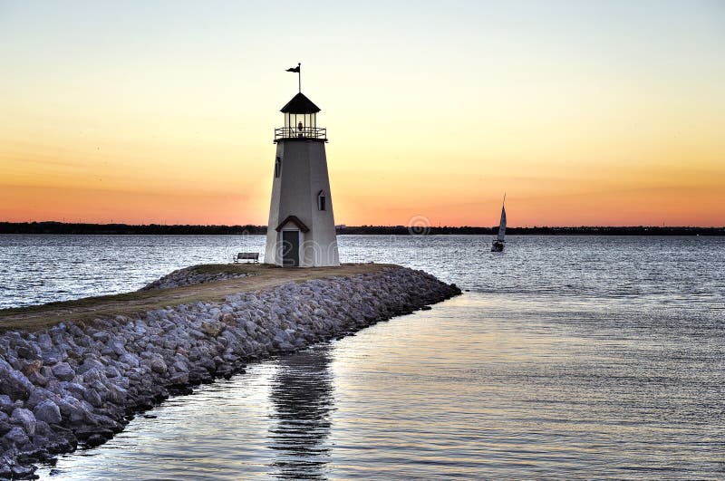 Coucher du soleil sur le lac Hefner à Oklahoma City, le phare dans le premier plan et un bateau à voile solitaire sur l'eau photographie stock libre de droits Coucher du soleil sur le lac Hefner à Oklahoma City, le phare dans le premier plan et un bateau à voile solitaire sur l'eau photographie stock libre de droits