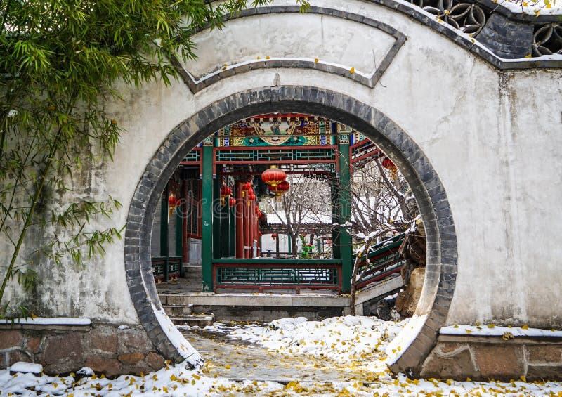 Couloir traditionnel historique derrière une porte de lune de Pékin, Chine en hiver avec la neige photographie stock libre de droits Couloir traditionnel historique derrière une porte de lune de Pékin, Chine en hiver avec la neige photographie stock libre de droits