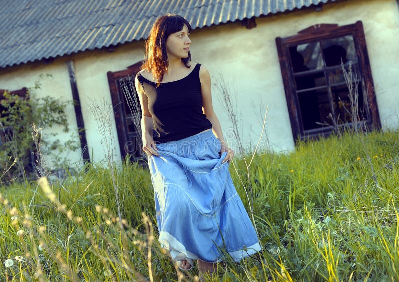 A woman with a long blue skirt walking in the grass outside an old house. A woman with a long blue skirt walking in the grass outside an old house.