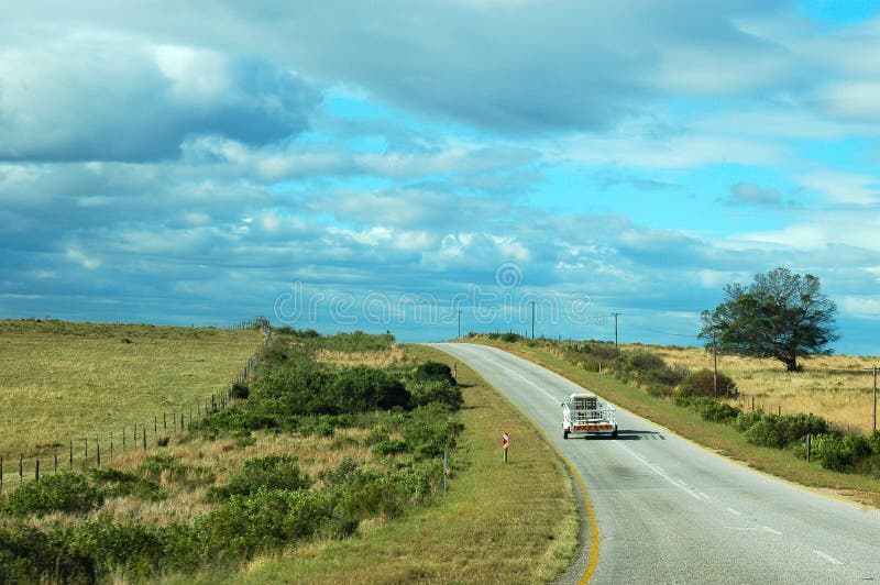 A lonely car with a trailer driving on an empty country road with tourists on vacation travelling in South Africa on a sunny summer day with blue sky and clouds. A lonely car with a trailer driving on an empty country road with tourists on vacation travelling in South Africa on a sunny summer day with blue sky and clouds