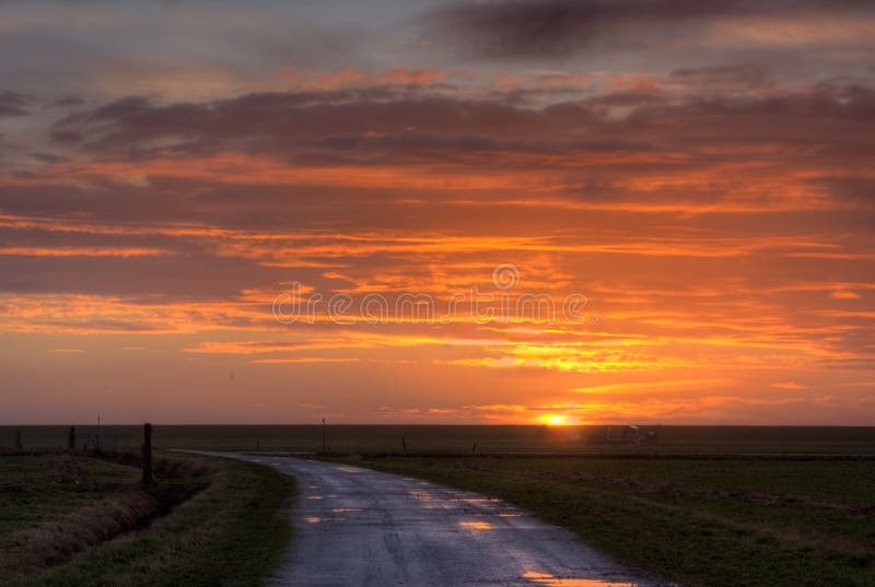 Bend country road in a flat land, leading towards a and a rising sun. Bend country road in a flat land, leading towards a and a rising sun