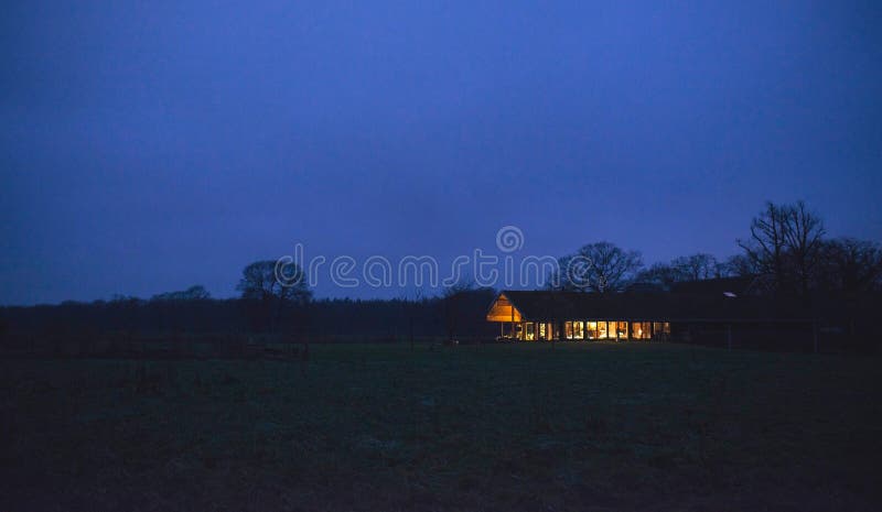 Countryside winter landscape with illuminated house at dusk.