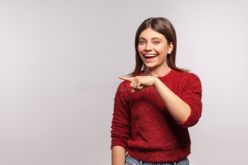 Afficher la publicité! portrait d'une jolie fille joyeuse en pull brun pointant l'espace vide et souriant photographie stock
