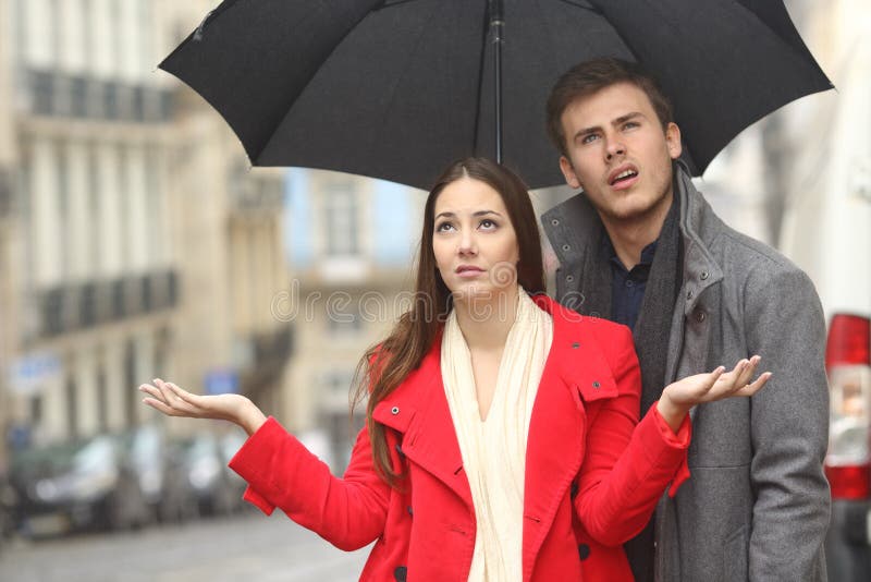 Portrait of a disgusted couple annoyed in a rainy day under the rain and an umbrella in winter