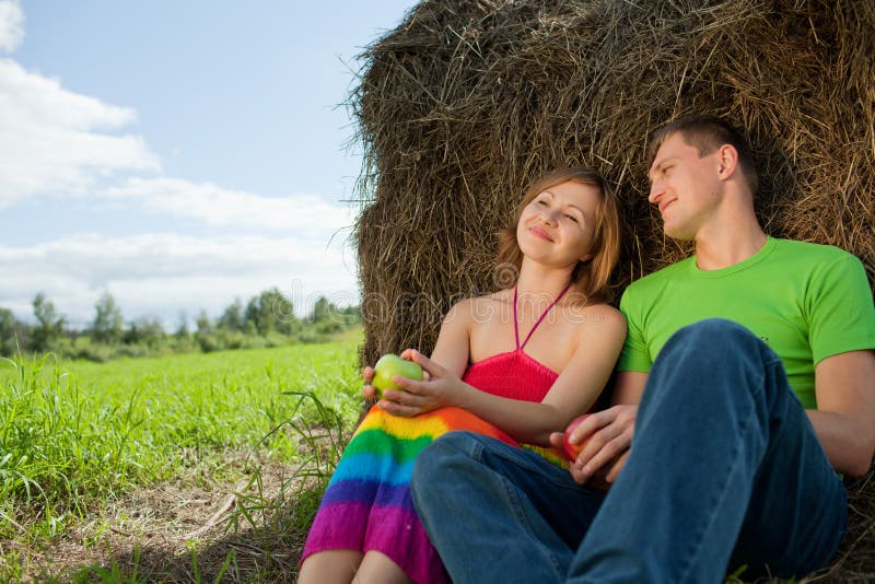 Couple with apples sitting on the grass hay stock photo