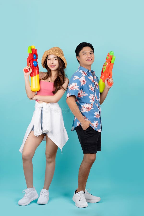 Couple asiatique en vêtements d'été avec pistolet à eau en fond bleu studio. ils sourient et regardent la caméra à songkran photo stock