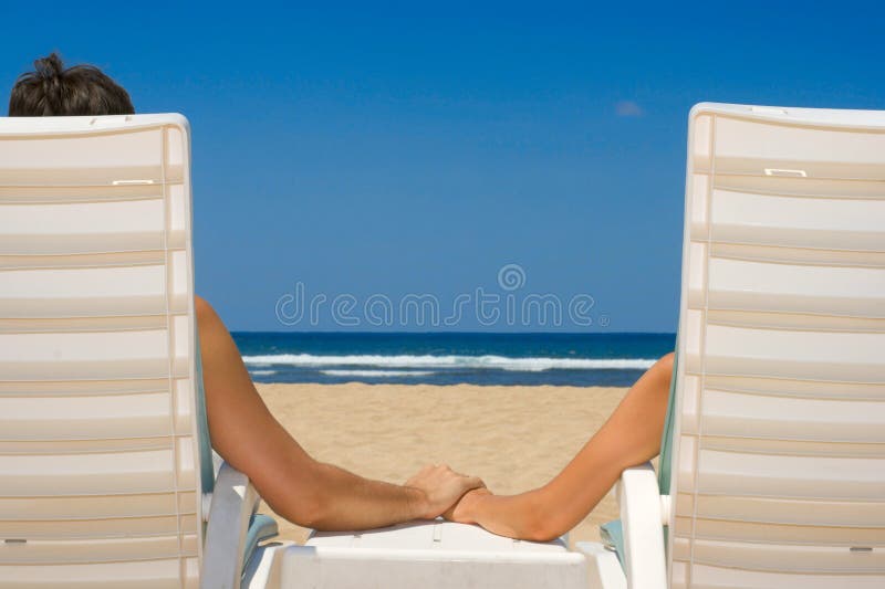 Couple in beach chairs holding hands near ocean