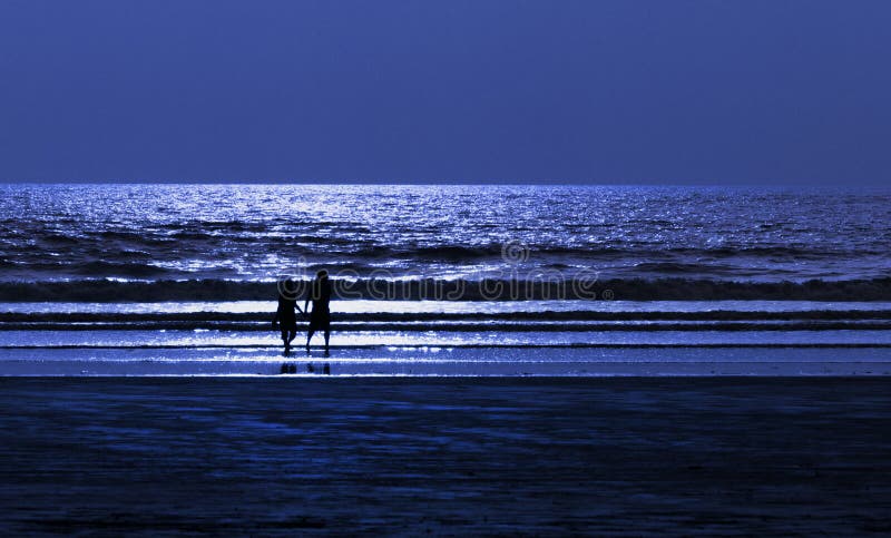 Una coppia romantica sulla spiaggia silhouette sotto la luce della luna e la notte blu di scena, le onde dell'oceano sfondo e sabbia.