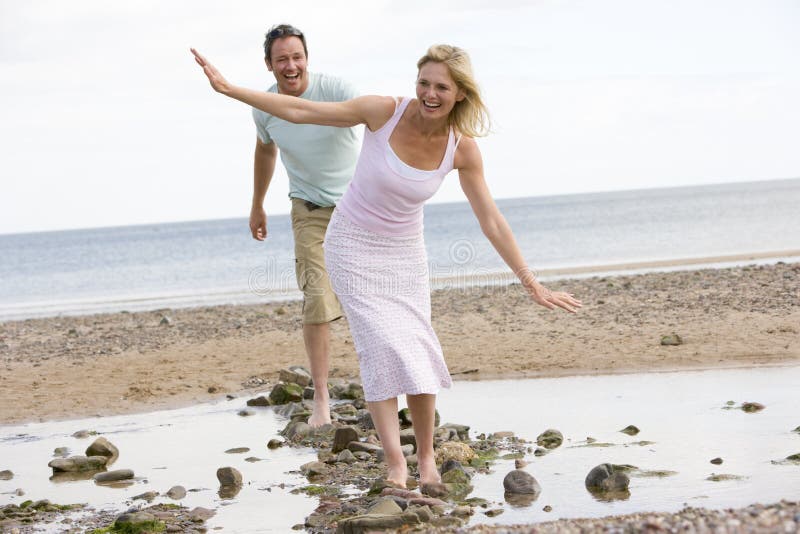 Couple at the beach walking on stones and smiling