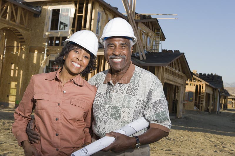Portrait of happy senior African American couple with blueprint in front of house under construction. Portrait of happy senior African American couple with blueprint in front of house under construction