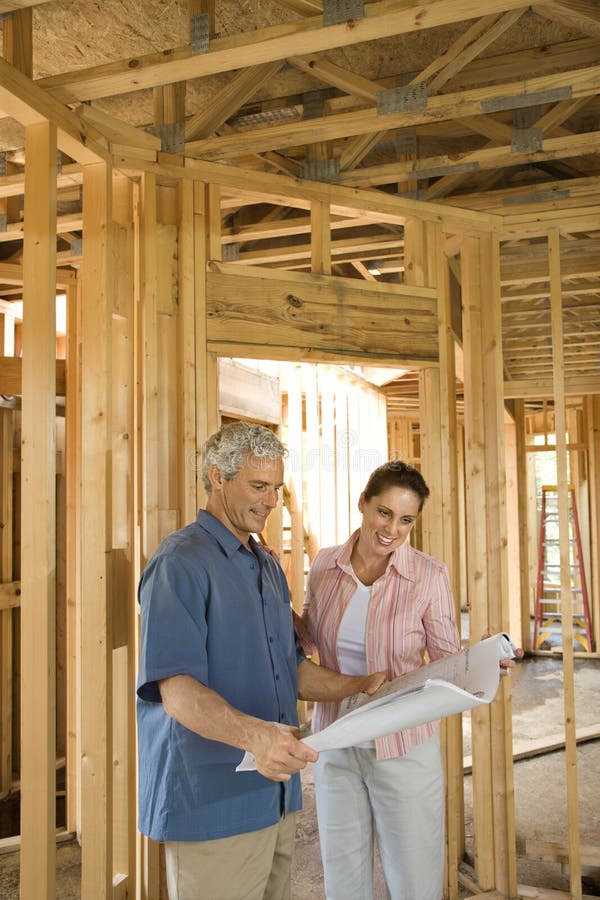 Couple go over home building plans at a construction site. Vertical shot. Couple go over home building plans at a construction site. Vertical shot.