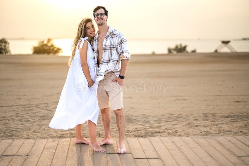 Couple in casual wear standing at the sea shore, hugging each other with love and looking at camera. Pregnant women and handsome men embracing at sidewalk. Couple in casual wear standing at the sea shore, hugging each other with love and looking at camera. Pregnant women and handsome men embracing at sidewalk.