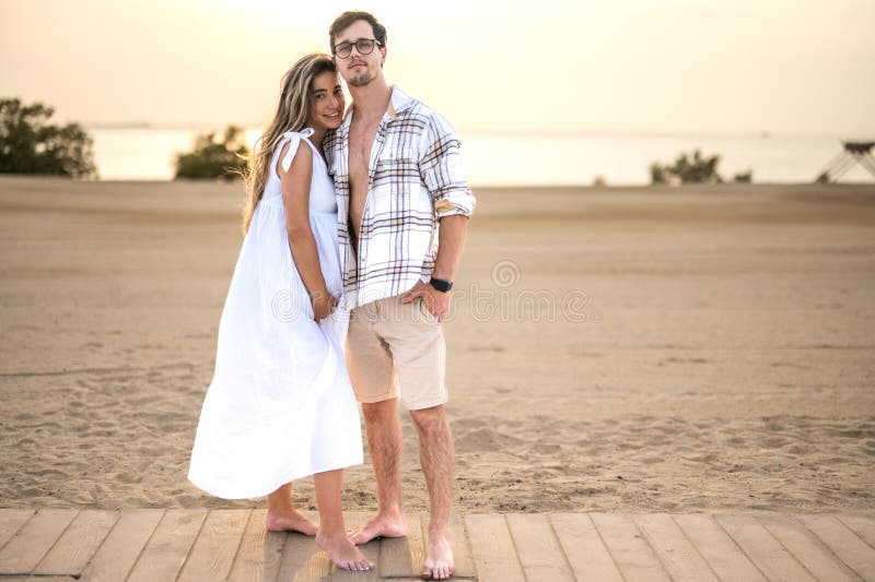 Couple in casual wear standing at the sea shore, hugging each other with love and looking at camera. Pregnant women and handsome men embracing at sidewalk. Couple in casual wear standing at the sea shore, hugging each other with love and looking at camera. Pregnant women and handsome men embracing at sidewalk.