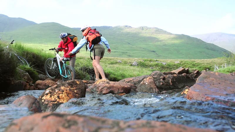 Couple crossing a stream together with their bikes