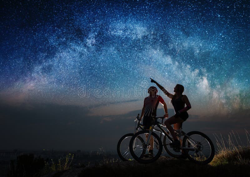 Couple cyclists with mountain bikes at night under starry sky