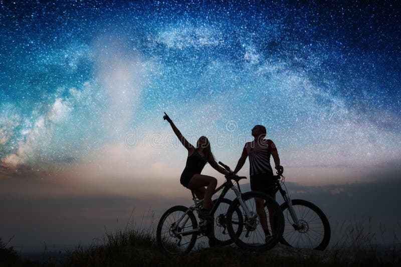 Couple cyclists with mountain bikes at night under starry sky