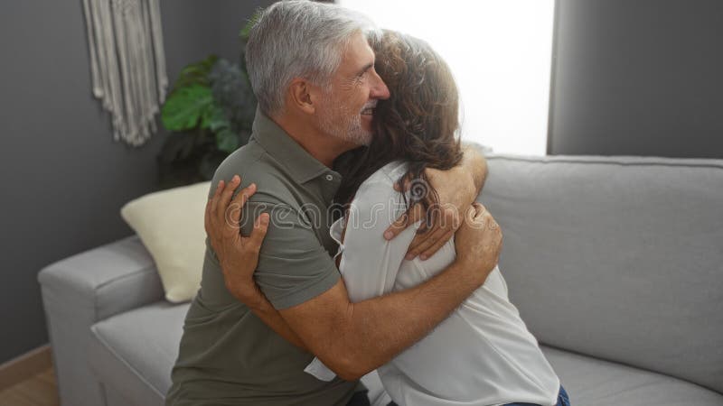 Couple d'âge moyen embrassant avec amour dans un salon confortable transmettant chaleur et affection entouré d'un décor chaleureux photo stock