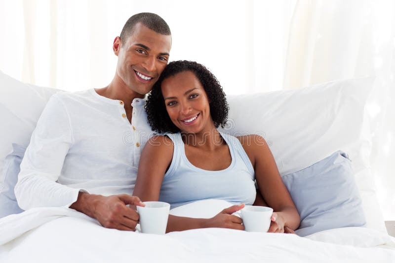 Smiling Afro-American couple drinking a coffee on their bed