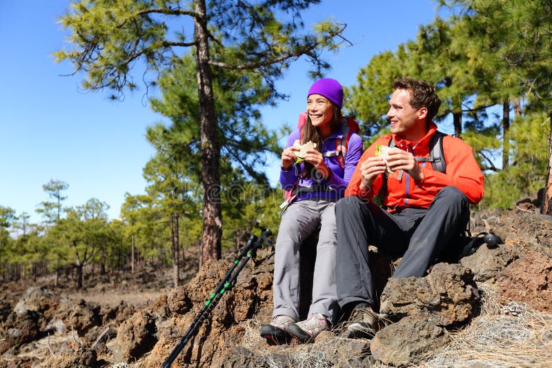 Couple eating lunch taking a break hiking enjoying sandwiches. Hikers living active lifestyle in mountain nature. Woman and men hiker sitting on hike on volcano Teide, Tenerife, Canary Islands, Spain.