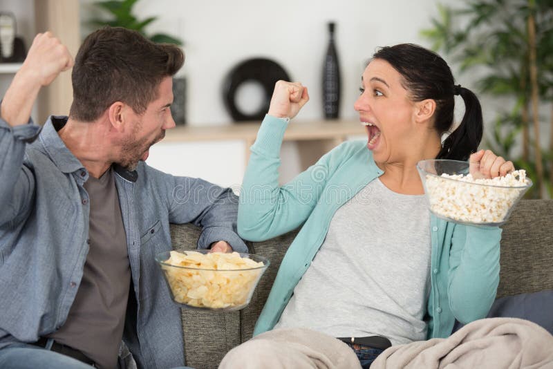 Couple Eating Popcorn Together and Watching Tv on Sofa Stock Photo