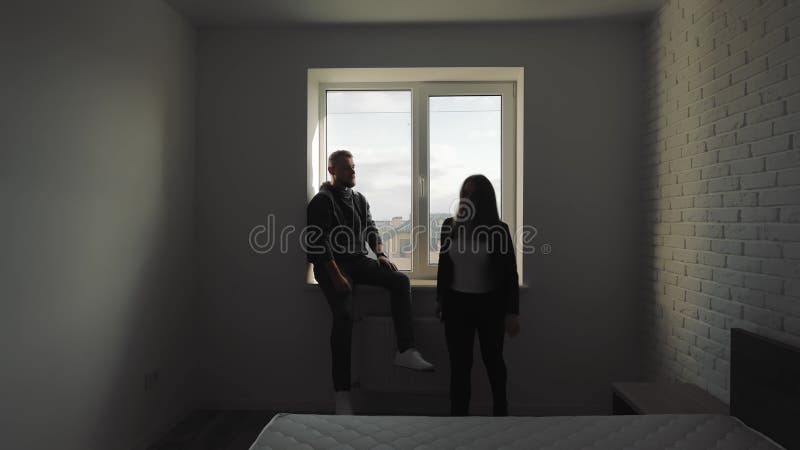 Couple en silhouette assis près d'une fenêtre dans une pièce minimaliste, un couple est assis sur le rebord d'une fenêtre minimali banque de vidéos