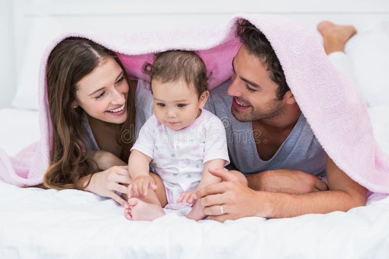 Couple Enjoying With Baby Under Blanket On Bed Stock Photo image
