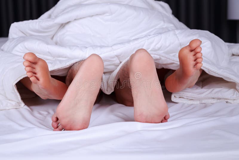 Couple feet seen from under blanket on bed stock image