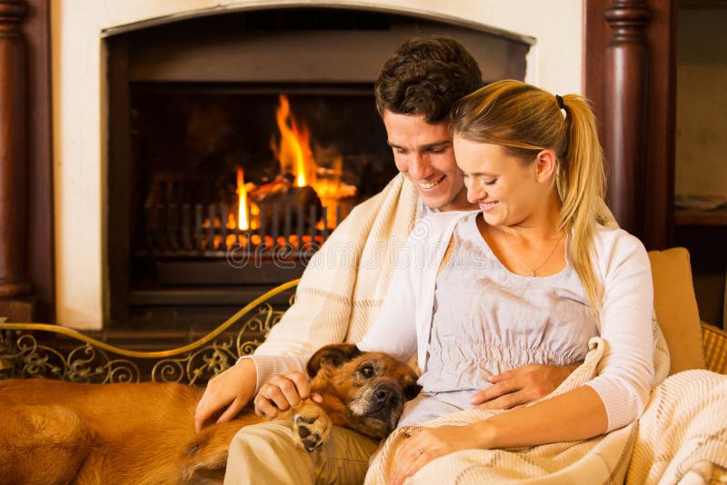 Beautiful young couple sitting by fireplace with their pet dog at home. Beautiful young couple sitting by fireplace with their pet dog at home
