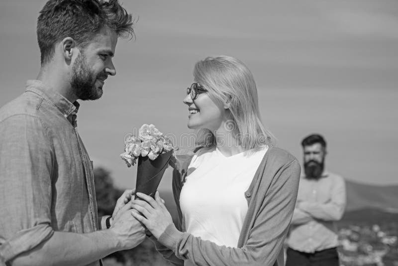 Couple with flowers bouquet romantic date. New love. Couple in love dating outdoor sunny day, sky background. Ex husband jealous on background. Ex partner watching girl starts happy love relations.