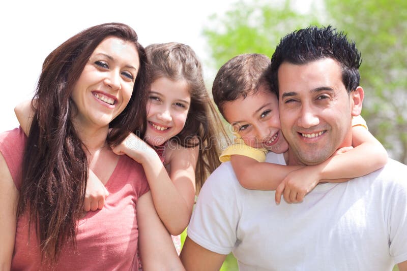 Couple giving two young children piggyback rides smiling, outdoor at the park