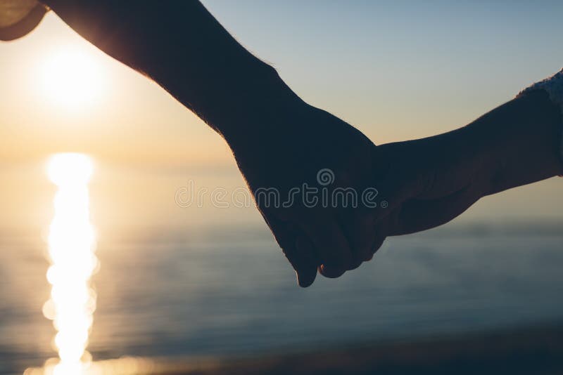 Couple of hands holding each other silhouette on a sky and sea background. People, black.