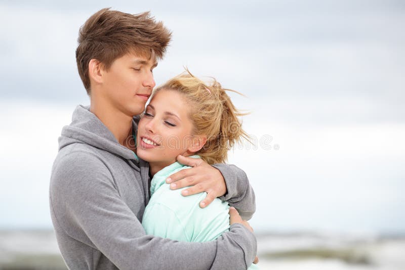 Couple embracing and having fun wearing warm clothes outside on coast behind blue sky. Couple embracing and having fun wearing warm clothes outside on coast behind blue sky