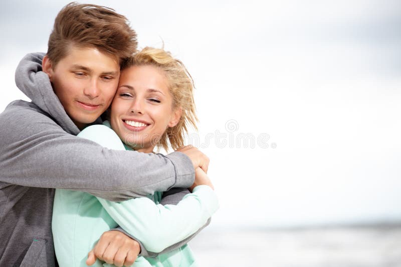 Couple embracing and having fun wearing warm clothes outside on coast behind blue sky. Couple embracing and having fun wearing warm clothes outside on coast behind blue sky