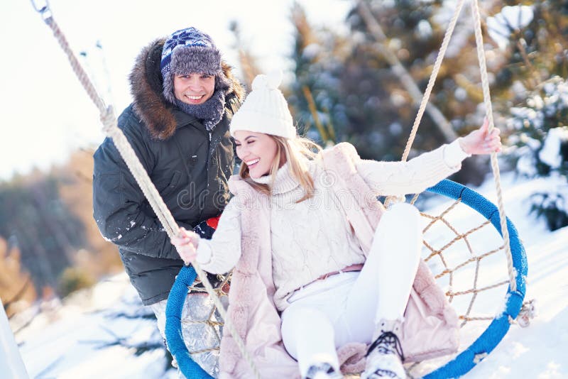 Couple having fun in winter snow on swing