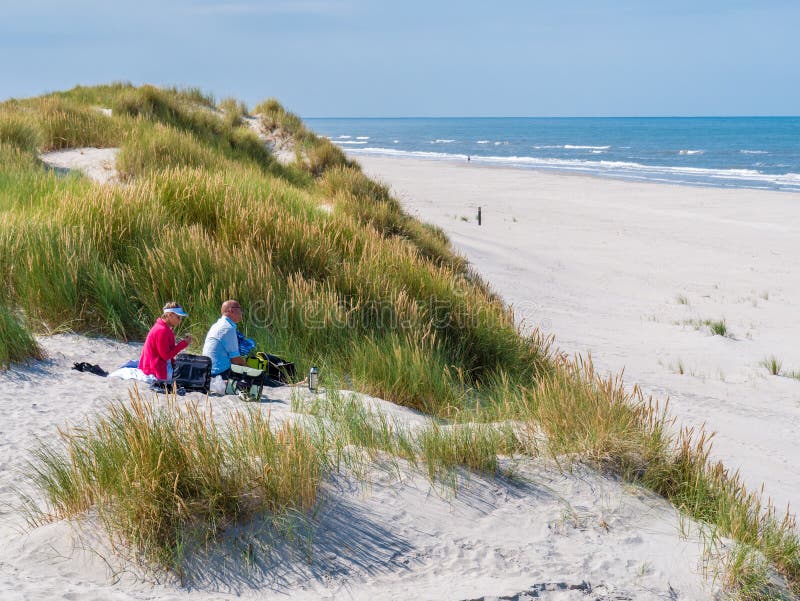 Couple having picnic on sand dune looking over beach and North Sea on West Frisian island Ameland, Friesland, Netherlands