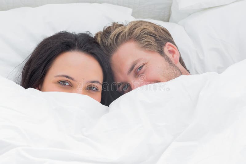 Couple hiding under the duvet in their bed