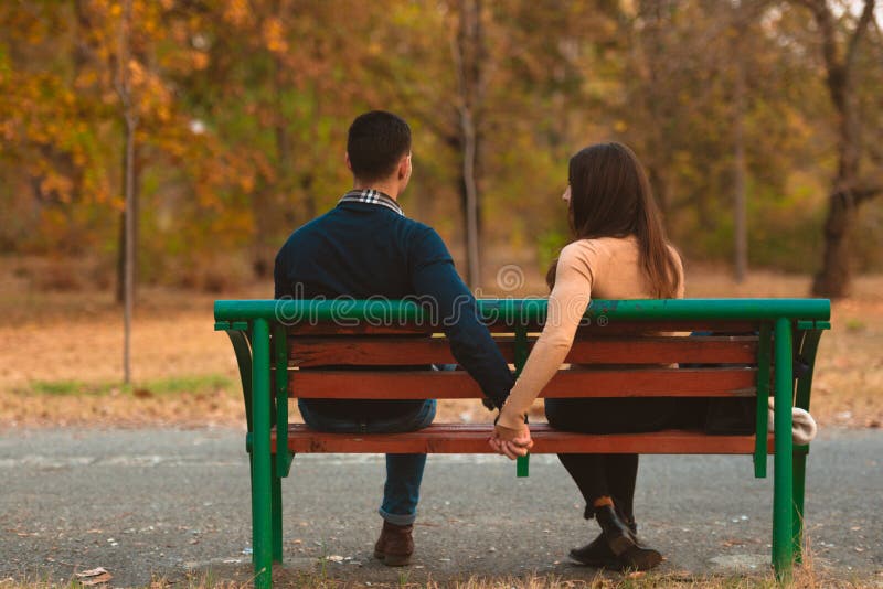 Couple holding hand and sitting on bench in autumn park