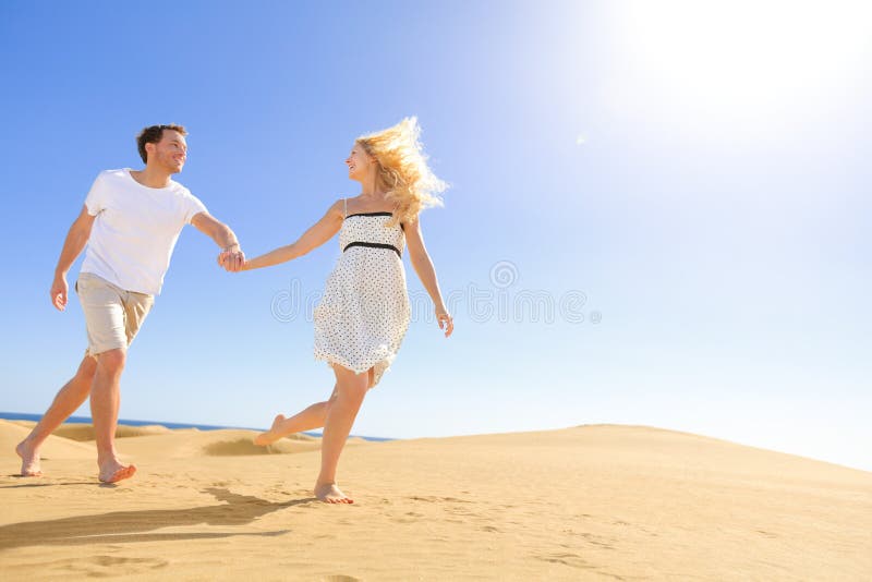 Couple holding hands running having fun under sun in playful and romantic relationship under sun and blue sky in desert. Two young lovers cheerful together on romance in summer. Joyful men and woman.