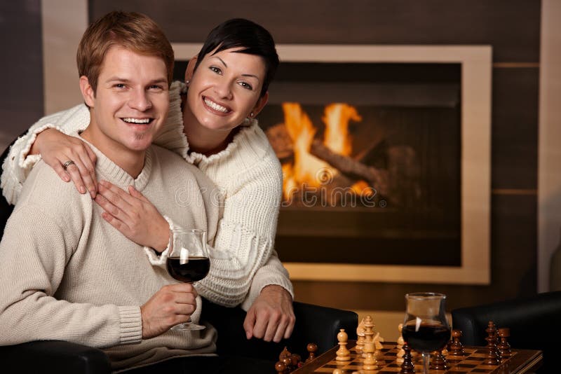 Happy young couple hugging in front of fireplace at home, looking at camera, smiling. Happy young couple hugging in front of fireplace at home, looking at camera, smiling.
