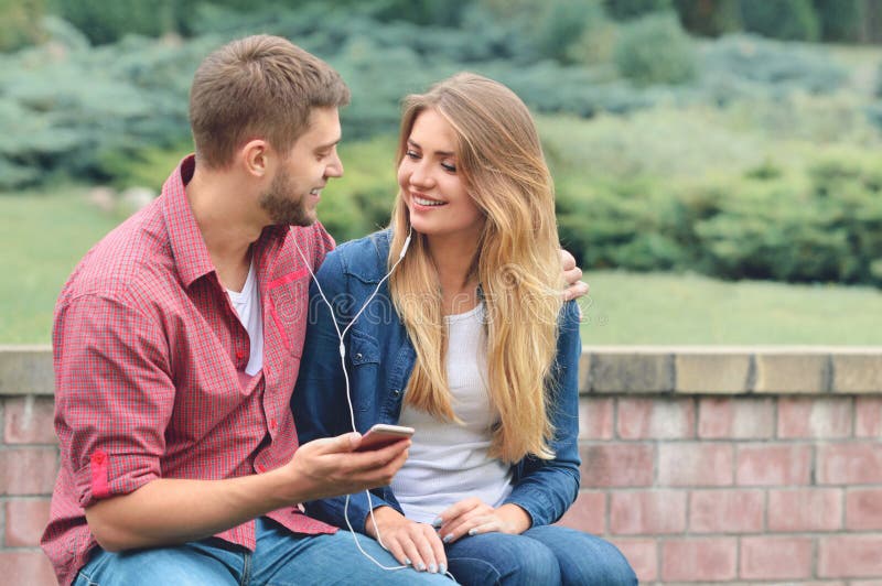 Couple listening to the music with earbuds from a smart phone in a park.